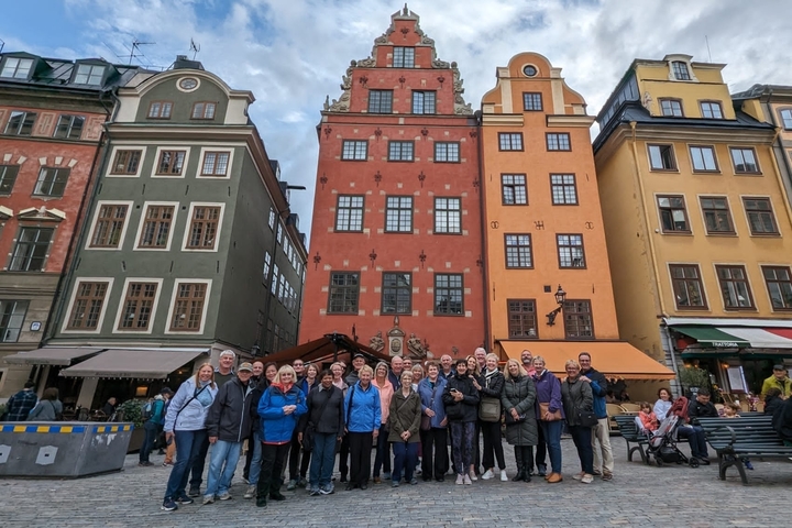 A group of people in front of colorful historic buildings in a European square.