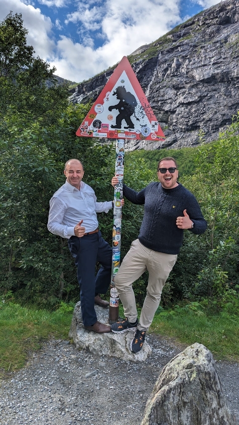 Two men posing with a decorated pole in a forest.