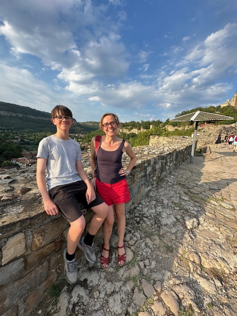 Two people relaxing on a stone wall with a scenic background.