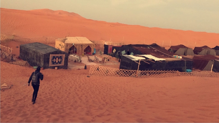       Desert camp with several tents and a person walking in the sand.
  