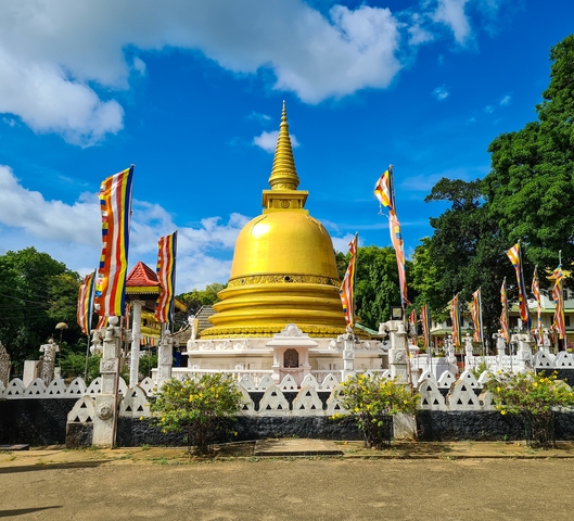 Golden stupa surrounded by colorful prayer flags and greenery.