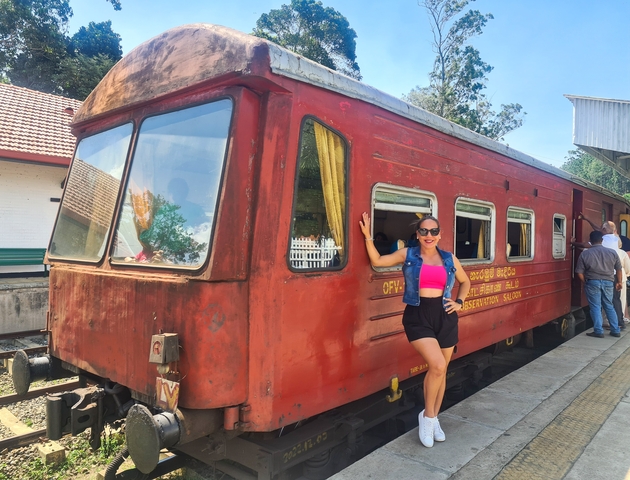 Person posing next to a red train carriage at a station.