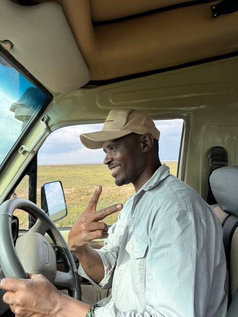       Smiling man in a safari vehicle making a peace sign gesture.
  