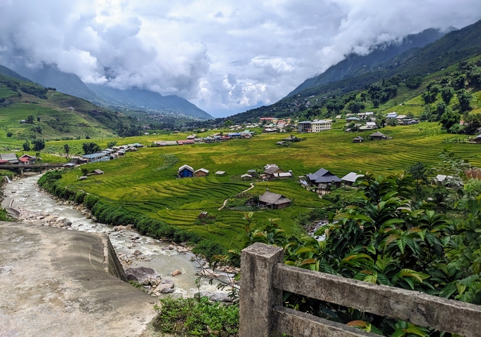       Valley with rice paddies and stream, surrounded by mountains.
  