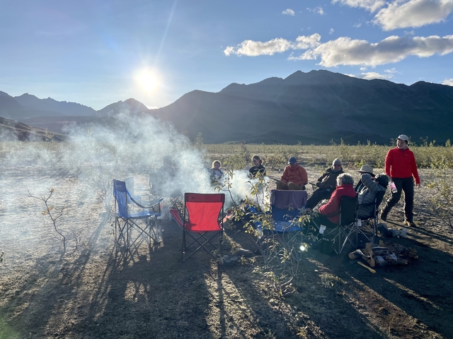      Group around a campfire with mountains in the background
  