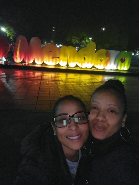       Two people in glasses posing in front of a multicolored sign
  