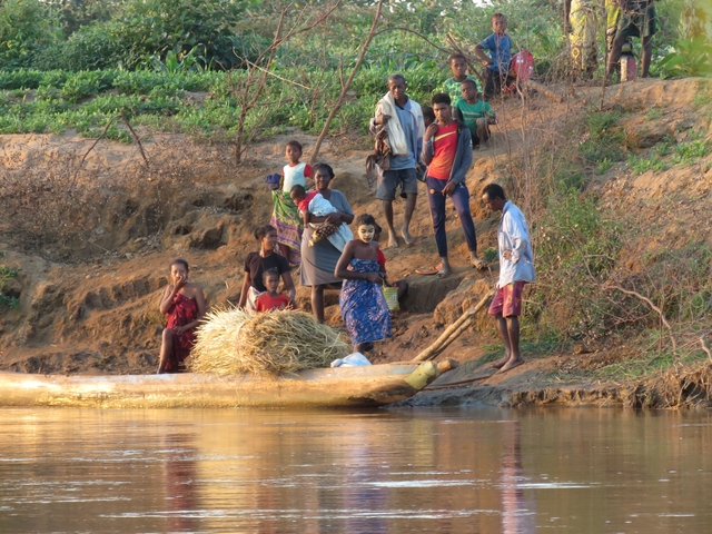       Group of people by a riverbank with a canoe.
  