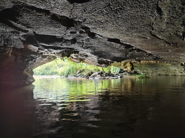 Inside a cave with a water body leading to an opening with trees outside.
