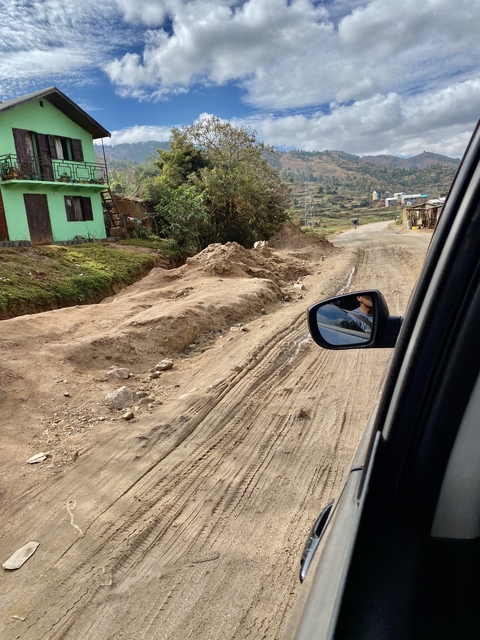 Dirt road with side mirror reflection, houses on the left.