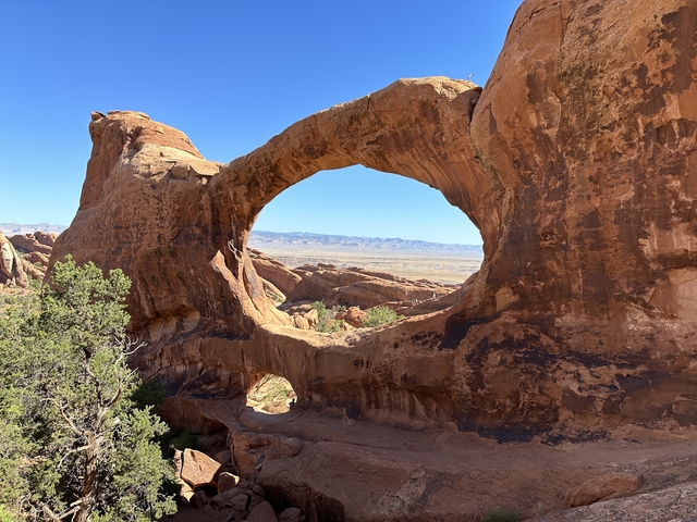       Rock formation with a large archway leading to a desert view.
  