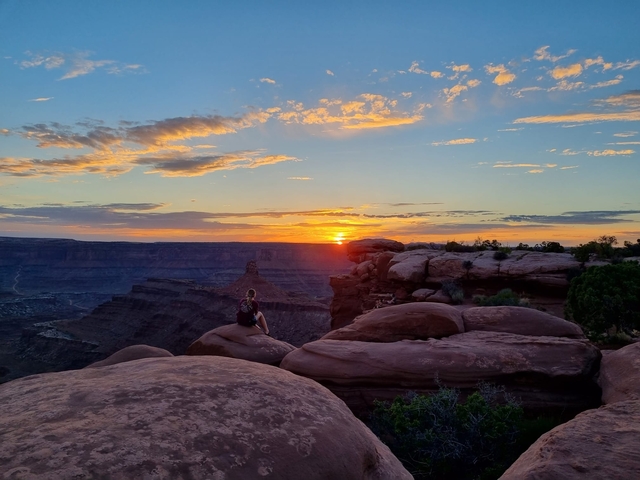       Person sitting on rocks enjoying the sunset view over a canyon.
  