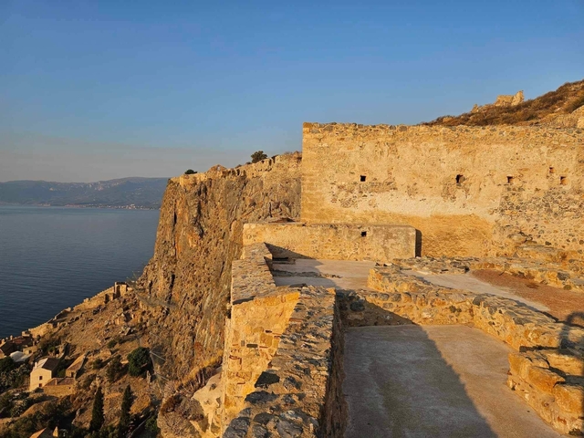       Stone fortifications along a cliff with a view of the sea.
  