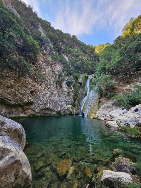       Person relaxing by a small waterfall and natural pool.
  
