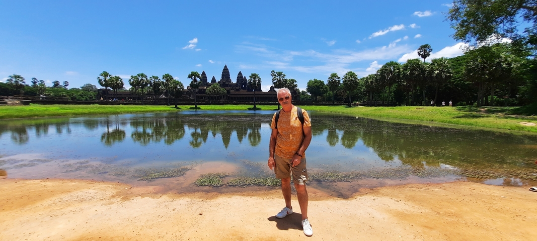       Person posing in front of Angkor Wat with reflective water in front.
  