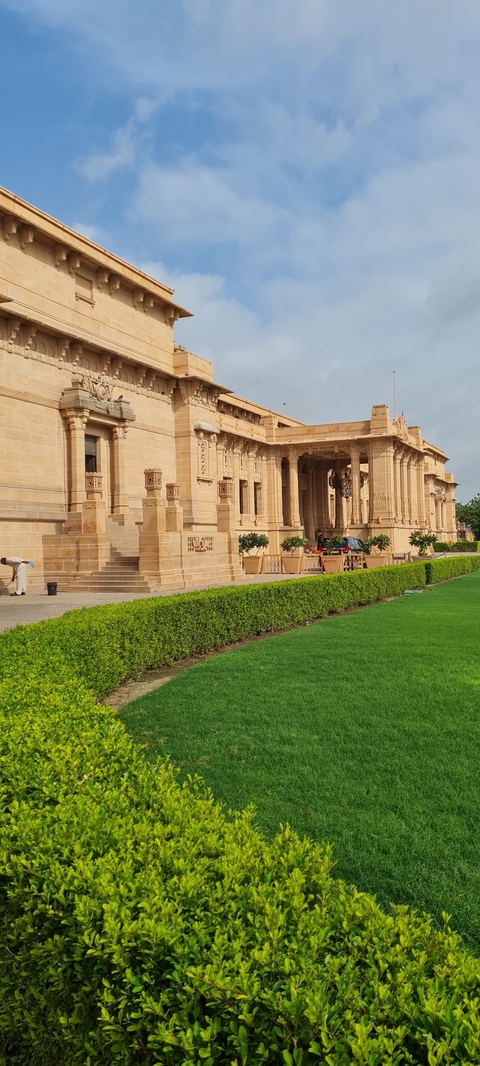       Grand entrance of a sandstone palace with well-maintained gardens.
  