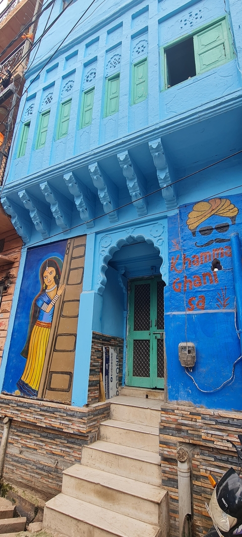       Blue-painted building with colorful murals and text.
  