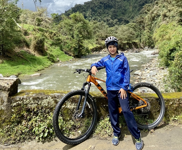 Person with a helmet and bicycle beside a scenic river.