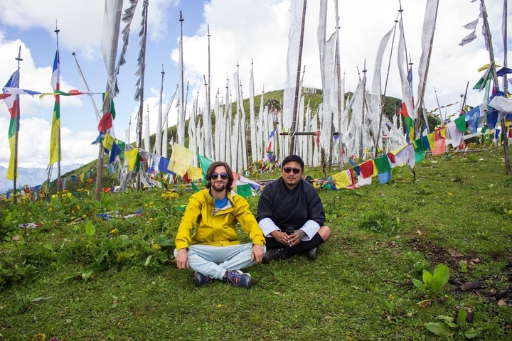 Two men sitting on a hill covered with prayer flags in Bhutan