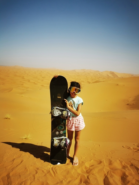       Child holding a sandboard in the desert, wearing goggles
  