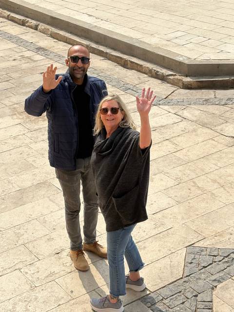       Two people posing and waving, standing on a stone path.
  