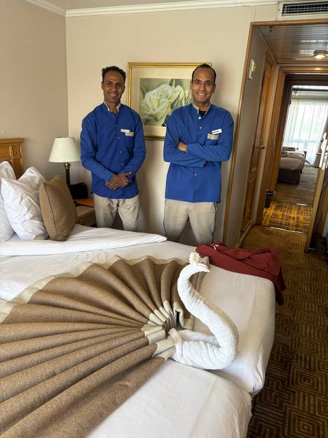 Two men in blue uniforms standing beside a bed.