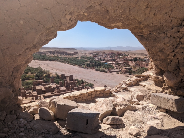       View through a stone window into a Moroccan valley and old buildings.
  