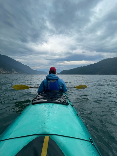 Person kayaking on a lake with mountains in the distance under an overcast sky.