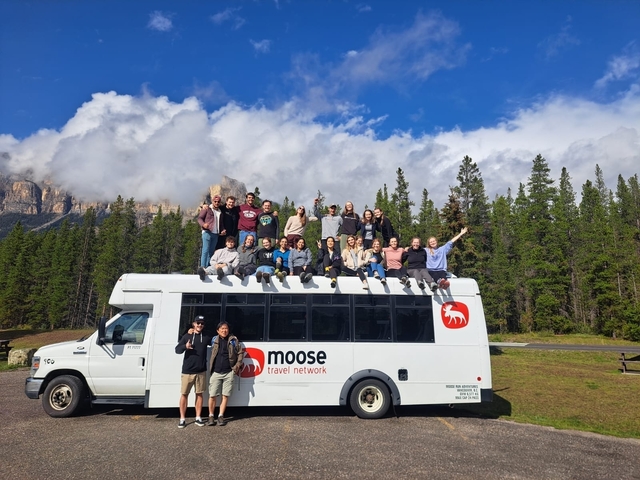 Group of people sitting on top of a travel bus with mountains in the background.