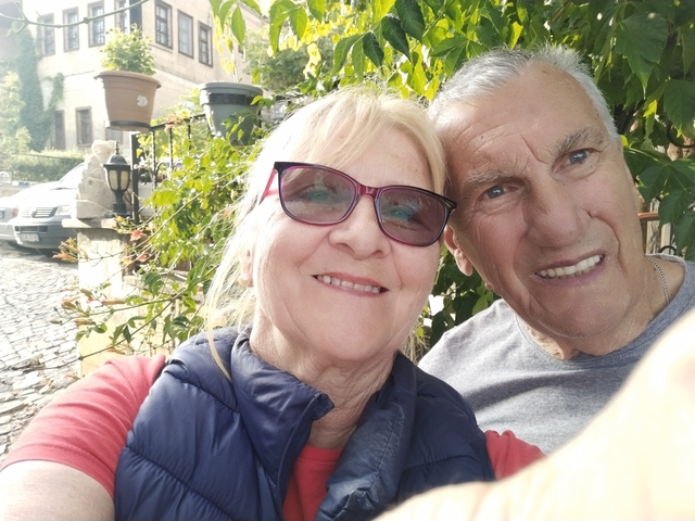       Close-up selfie of a couple outdoors among foliage.
  