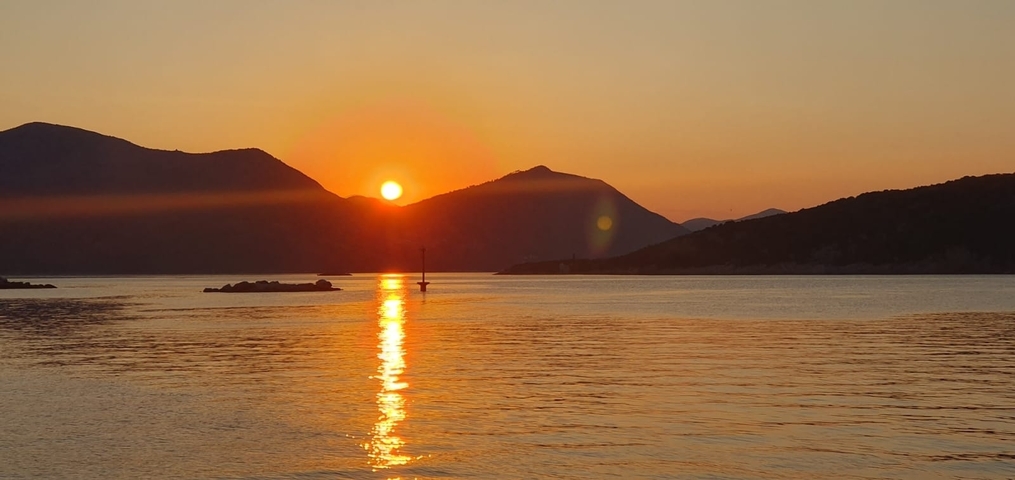Sunset over a calm sea with hills in the background.