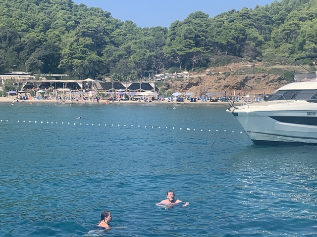      A person swimming in the sea near a yacht with a beach in the background.
  