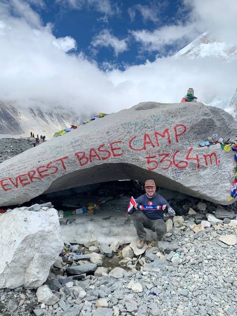 A person leaning on a rock with 'Everest Base Camp' written on it.