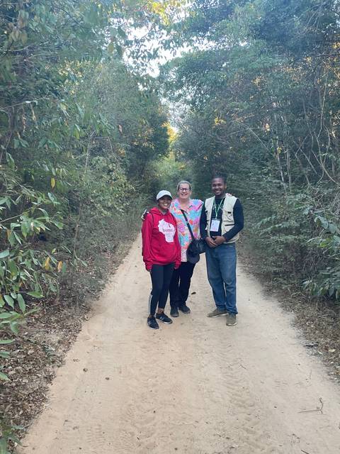 Three people standing on a sandy path in a forest.