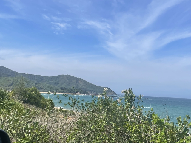Coastal scene with ocean and mountains under blue sky.