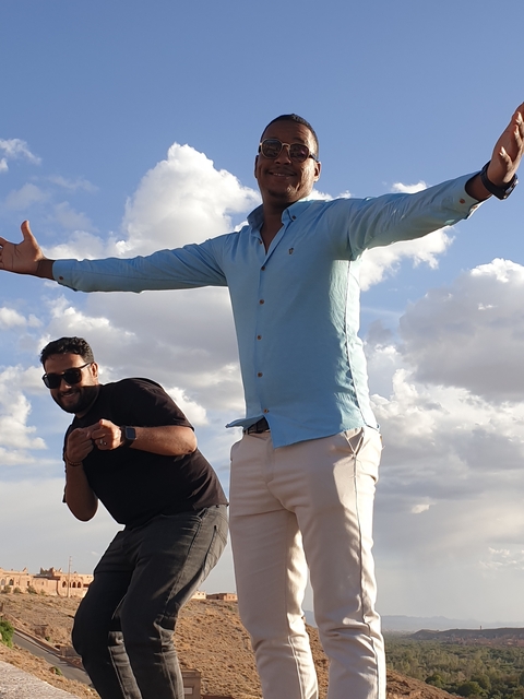 Two people posing outdoors with a cloudy sky background.