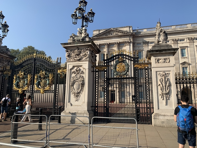 View of the gates of Buckingham Palace with people passing by.