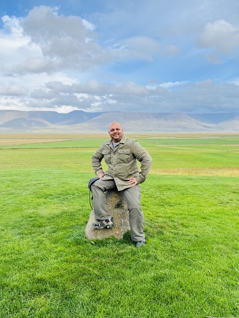       Man sitting on a rock in a vast green landscape.
  