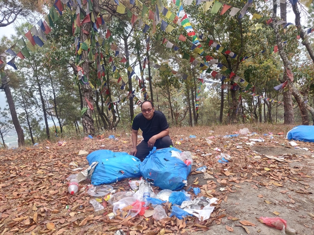 Man squatting among blue bags with trash collected in a forest.