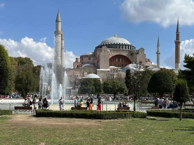       Large mosque with a fountain and park in front.
  