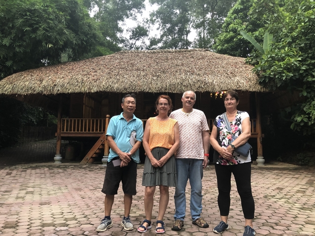       Four people posing in front of a building with a thatched roof.
  