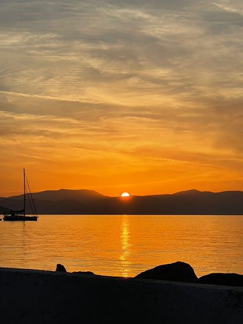 Sunset over the sea with mountains in the background and a sailboat.