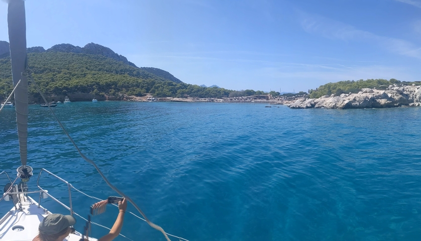 View from a sailboat towards a coastline with blue waters.