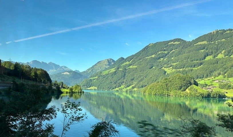 Lush green valley with mountains and a reflective lake.