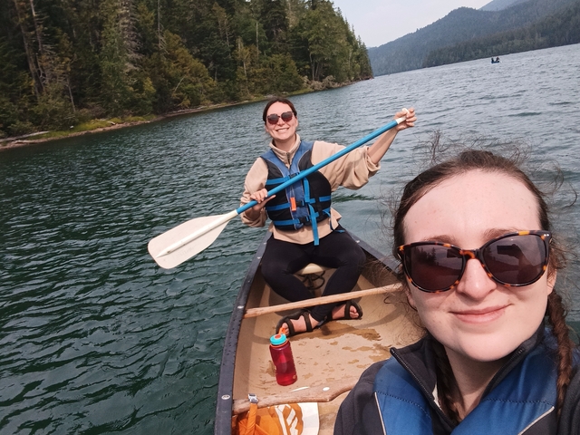       Women canoeing on a lake with trees in the background.
  