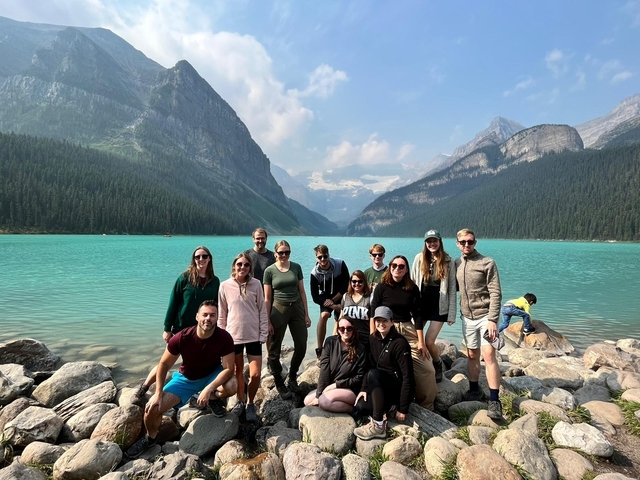       Group of people posing in front of a turquoise lake and mountains.
  