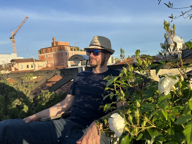 Man wearing sunglasses and a hat sitting above a city skyline.