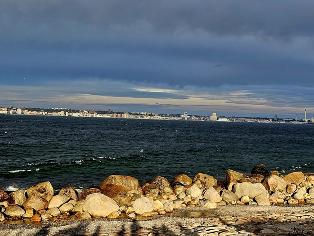 Rocky coastline with a cityscape seen across the water.