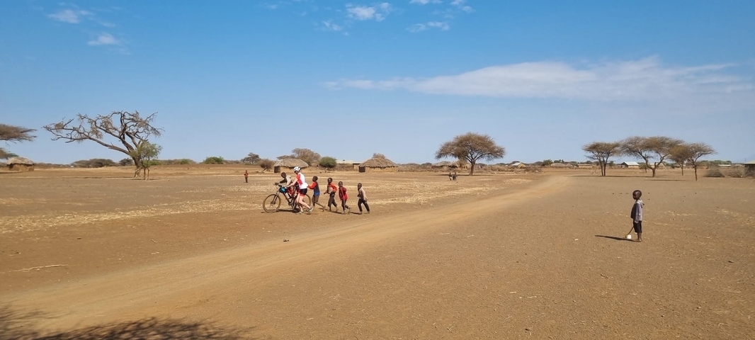       Group of people and children on dirt road in rural setting.
  