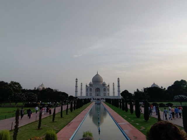       The Taj Mahal with visitors lining the gardens and reflecting pond.
  