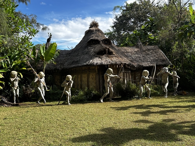 A traditional hut with figures in front holding spears.